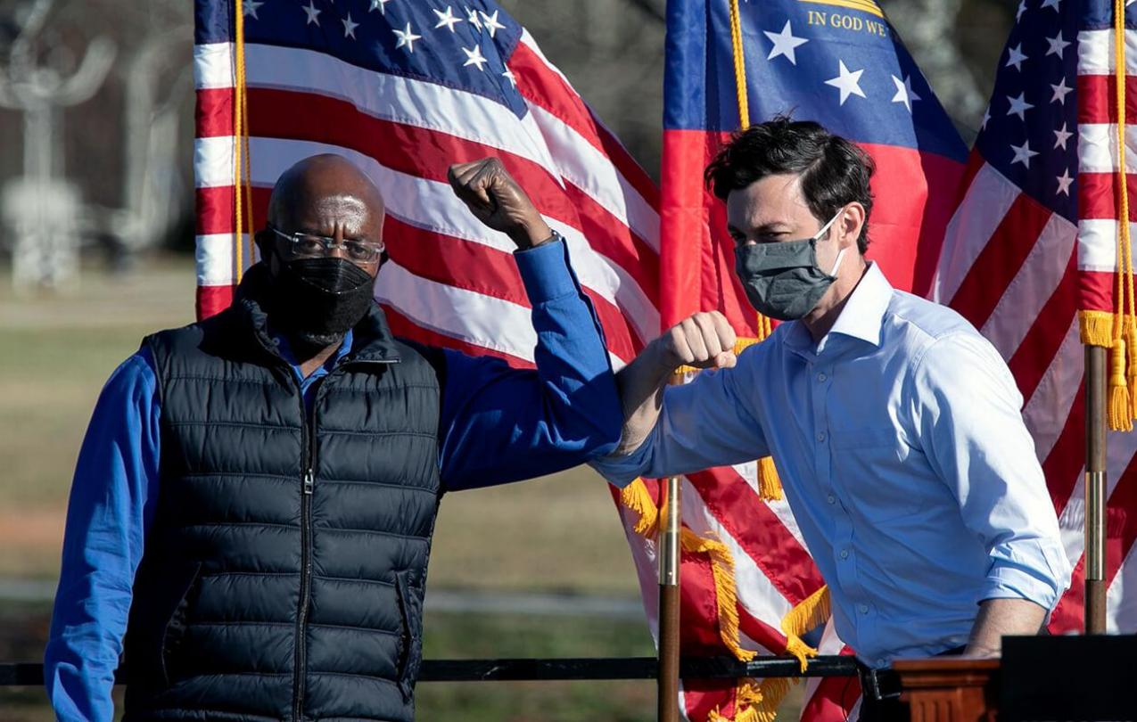 Democratic U.S. Senate candidates Raphael Warnock (L) and Jon Ossoff bump elbows during an outdoor drive-in rally in Conyers, Georgia.